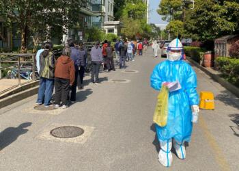 A medical worker in a protective suit walks past a line of people waiting to take nucleic acid test at a locked down residential area, following the coronavirus disease (COVID-19) outbreak in Shanghai, China April 7, 2022. REUTERS/David Stanway