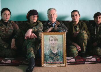 Programme Name: Anna: The Woman Who Went to Fight ISIS - TX: 03/07/2019 - Episode: n/a (No. n/a) - Picture Shows: Dirk Campbell holding a portrait of his daughter Anna, with International YPJ soldiers  - (C) BBC - Photographer: Seb Rabas