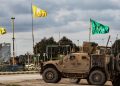 A patrol of US military vehicles is seen near the flying yellow flags of the Syrian Democratic Forces (SDF) and green flags of its constituent Women's Protection Forces (YPJ) in the town of Tal Tamr in the northeastern Syrian Hasakeh province along the border with Turkey on February 8, 2020. (Photo by Delil SOULEIMAN / AFP) (Photo by DELIL SOULEIMAN/AFP via Getty Images)
